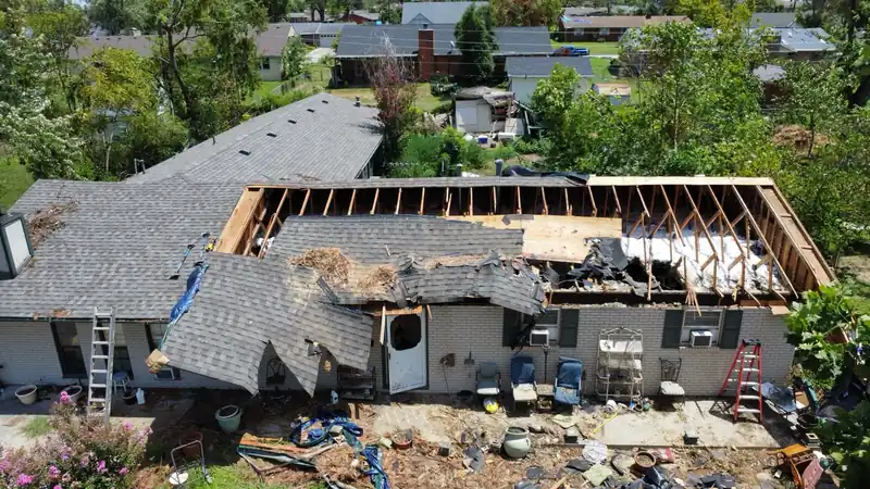 Drone view of a storm-damaged house with the roof torn open to the rafters and debris in the yard