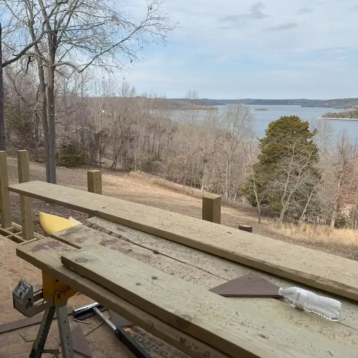 Deck boards being cut on sawhorses on a hillside deck with a lake view