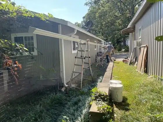 Gutter work on a grey-sided house with a ladder up