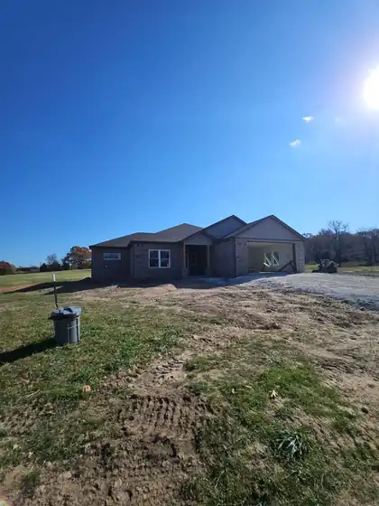 Finished new-build brick home on a raw lot under a wide sky
