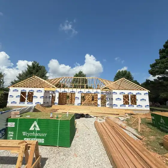New-construction house framed and wrapped with roof trusses up and lumber staged on gravel