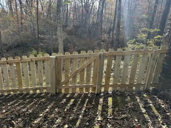 New wood picket fence with a gate along a wooded lot