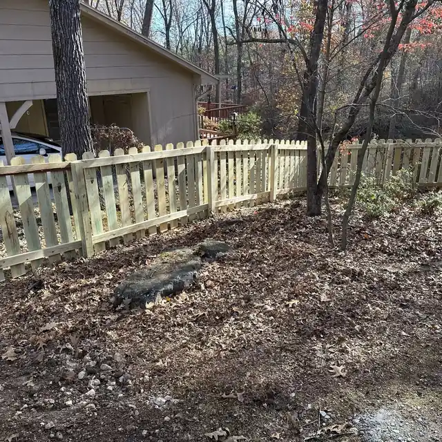 New picket fence across a wooded backyard