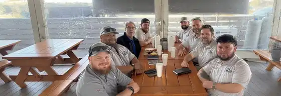 The Elite Home Solutions crew of eight in matching grey company shirts gathered around a picnic table