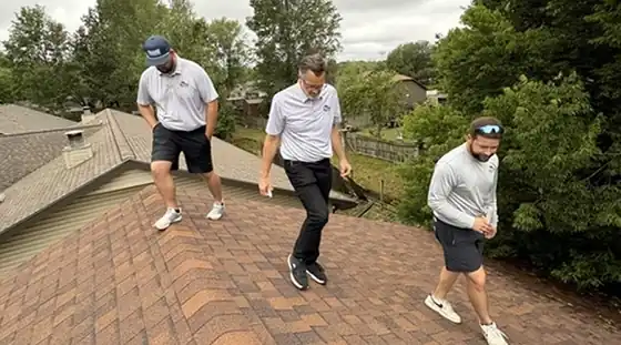 Three Elite Home Solutions crew members in company polos walking a shingled roof during an inspection